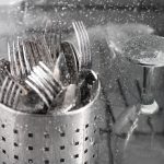 Some utensils and glasses are being washed inside of a dishwasher.